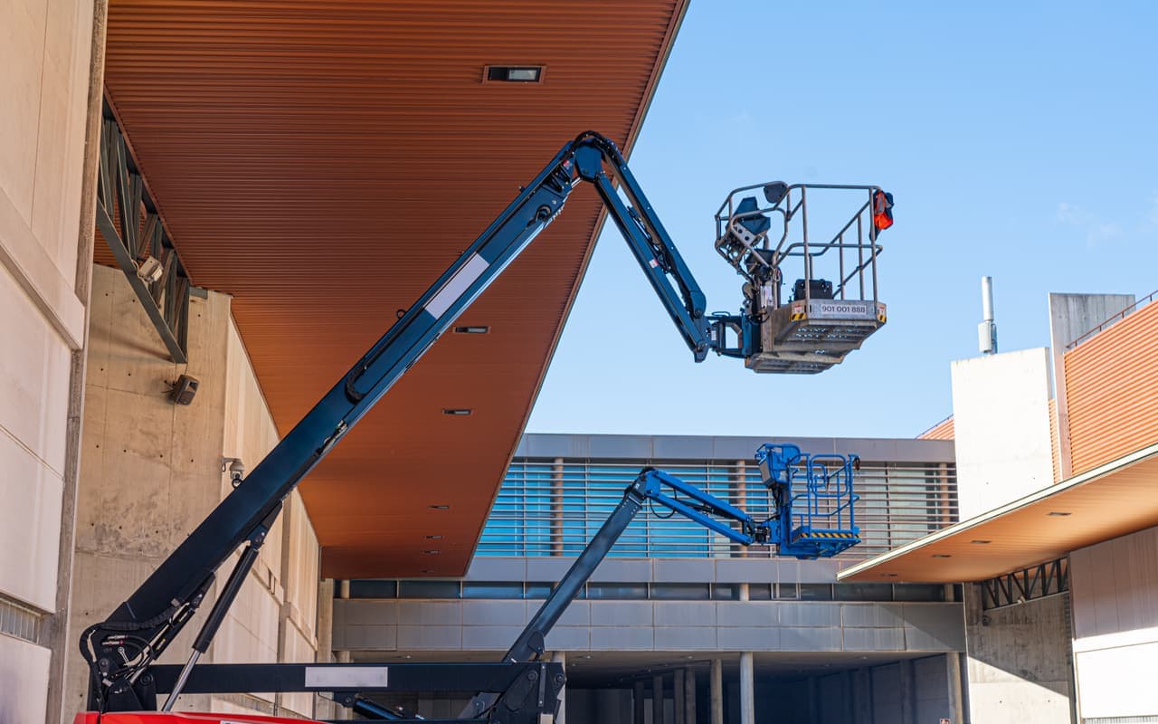 Twee knikarmhoogwerkers aan het werk bij een modern bedrijfspand